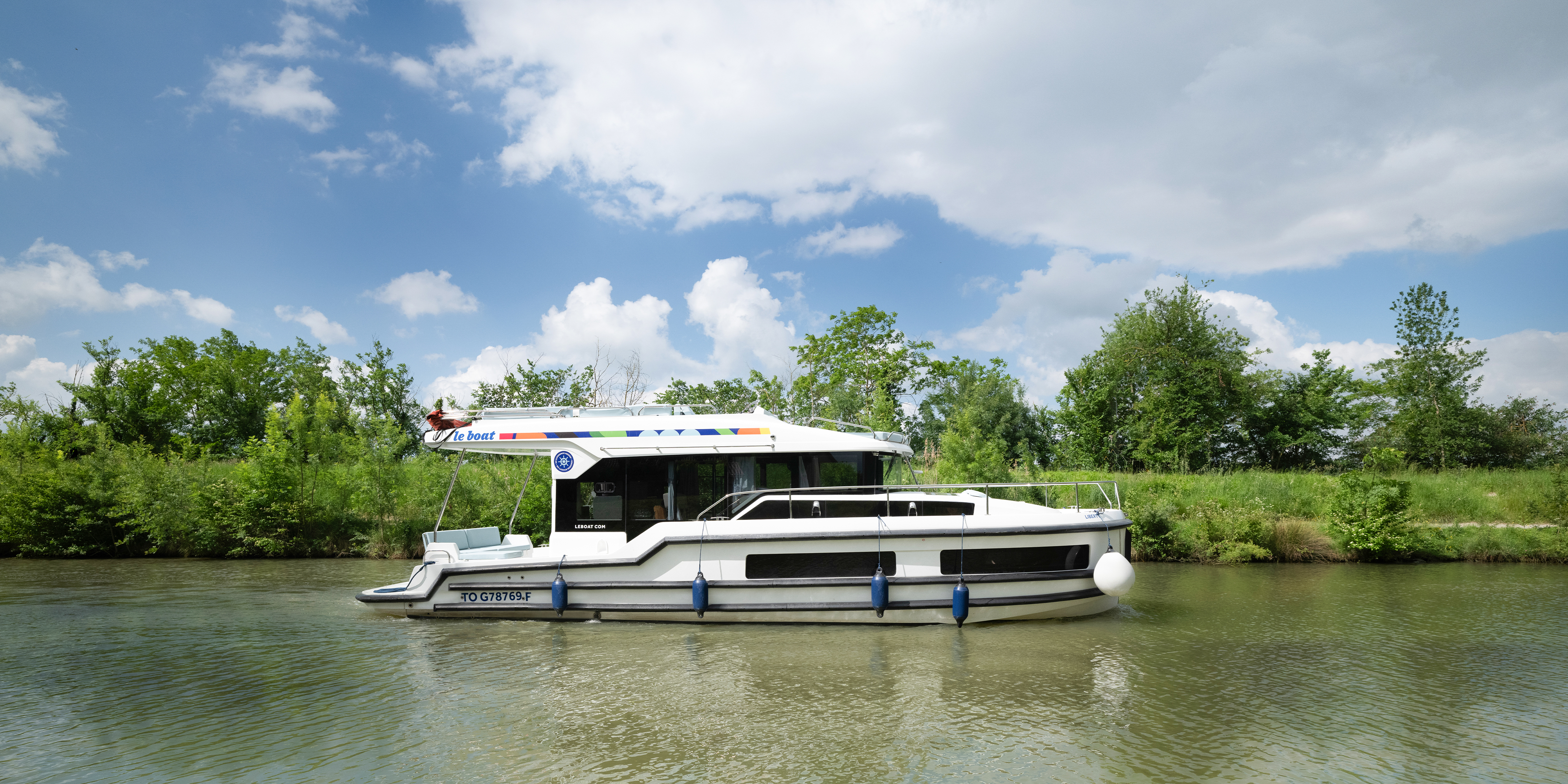 Bateau Liberty de Le Boat naviguant sur une voie d'eau bordée de végétation